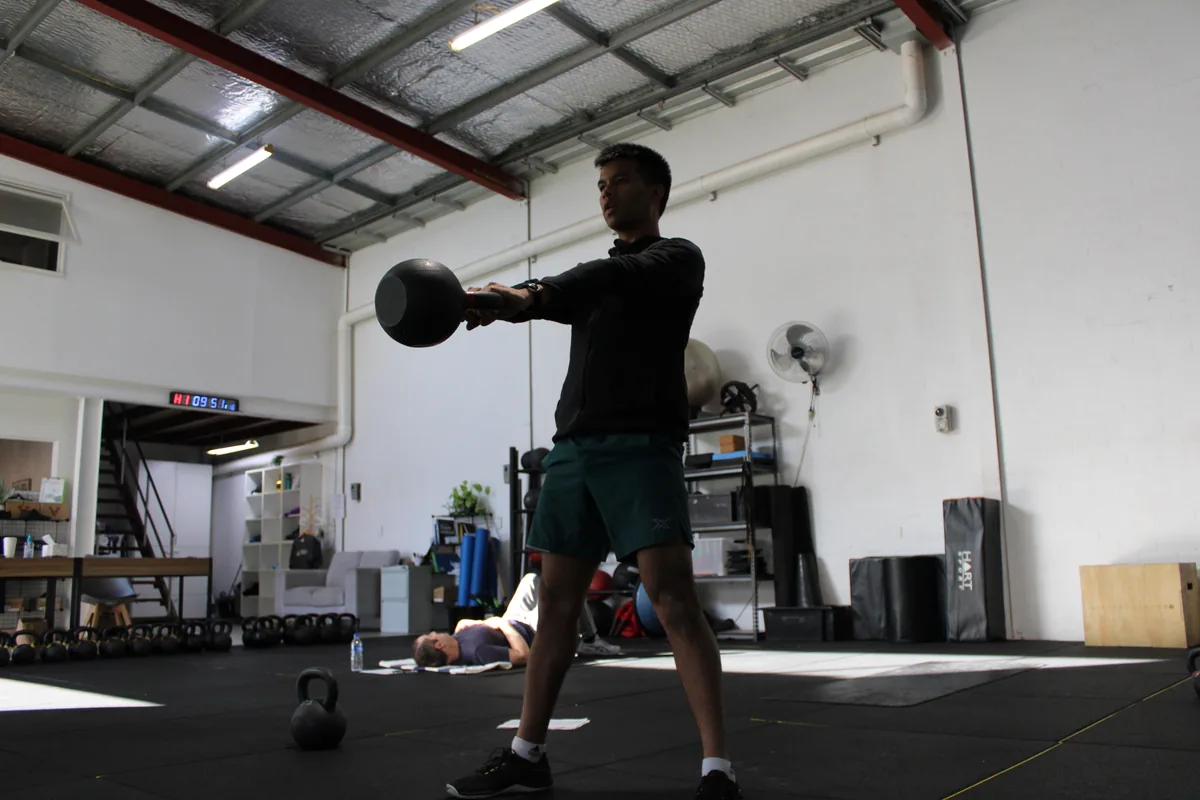 Person performing a kettlebell exercise in Adaptive's strength training environment in Booragoon.